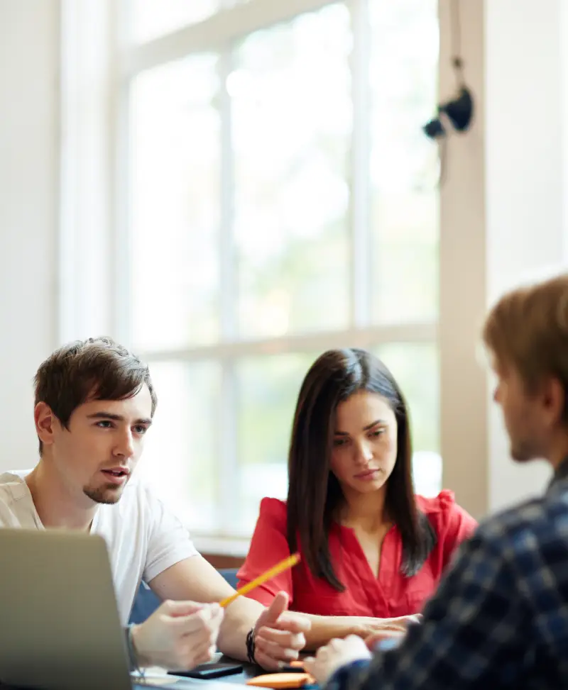 A person wearing headphones holds a paper comparing 'Past Simple' and 'Past Continuous' tenses, seated at a desk with study materials.